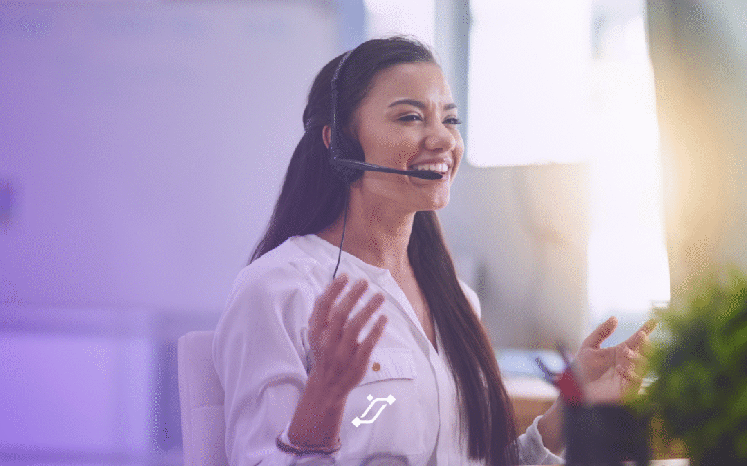 A smiling woman wearing a headset sits at a desk, gesturing with her hands as she assists a customer in a brightly lit office environment, demonstrating the ease of TechPOS inventory management.